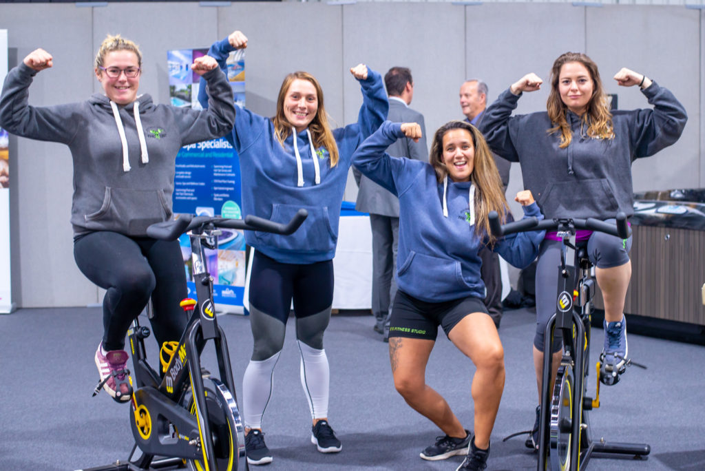 Women on exercise bikes at CIOS GrowthHub GrowthFest event. By editorial photographer Claire Wilson.