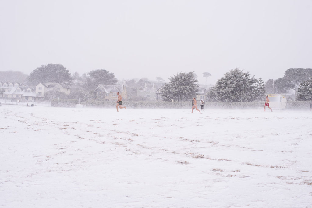 Students run across a snow covered beach at Falmouth